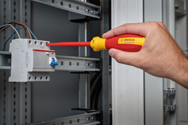 Person uses an insulated screwdriver to tighten a screw in an electrical panel.