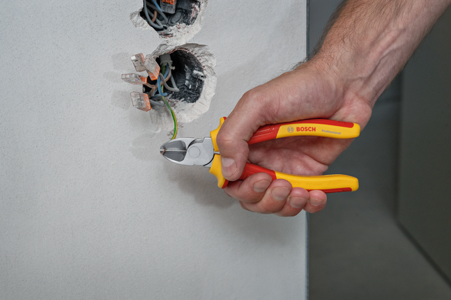 Person uses insulated pliers to cut a green wire from an electrical wall socket.