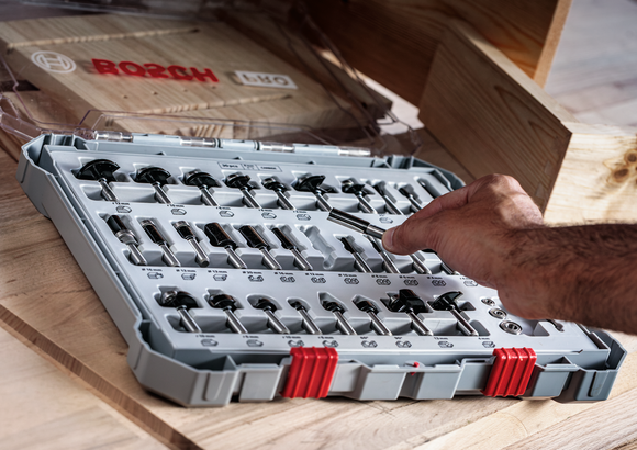 Person selects a drill bit from an organized set on a wooden table.