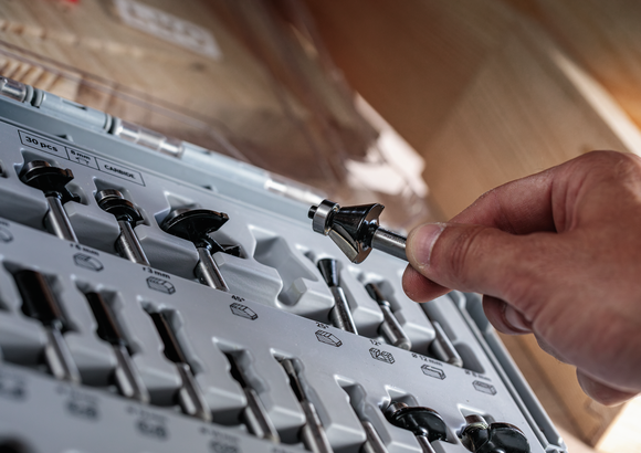 Person holding a router bit above a set of assorted drill bits in a case.