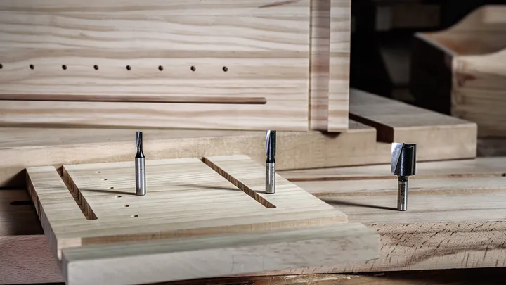 Object #200587640: 7437772_app_web_02 Three router bits displayed on a wooden workbench with machined wood pieces.