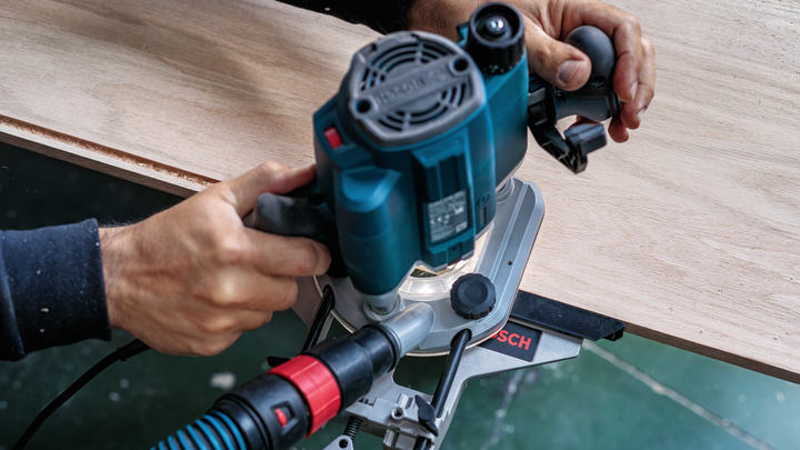 Object #200587642: 7437772_app_web_04 Person guides a power tool with dust extraction while shaping the edge of wood.