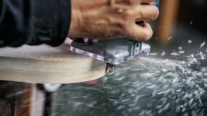 Object #200587669: 7437775_app_web_01 Person guides a power tool along wood edge as shavings scatter.