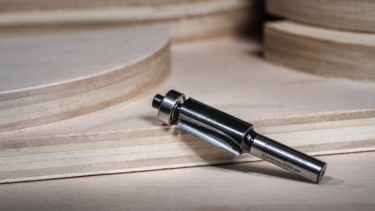 Router bit placed on a wooden surface near stacked plywood sheets.