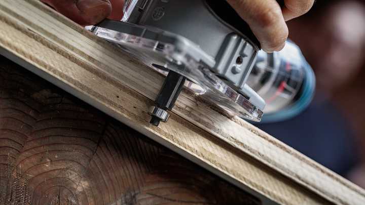 Object #200587676: 7437775_app_web_08 Person trims a wooden board edge with a handheld router tool.