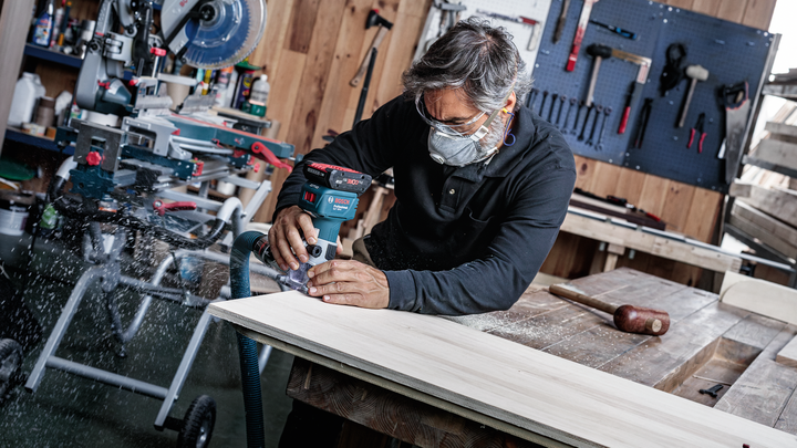 Object #200587677: 7437775_app_web_09 Person wearing safety equipment using a cordless router on a wooden board.