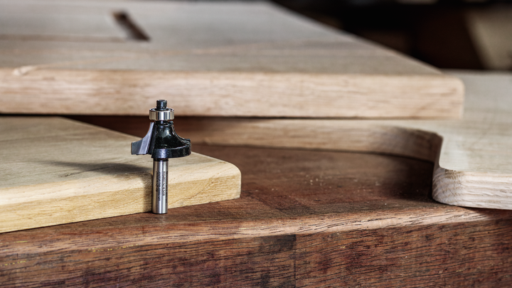 Object #200587696: 7437778_app_web_02 Router bit resting on a wooden workbench beside cut and shaped wood panels.