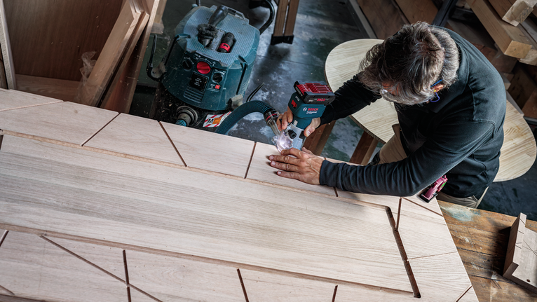 Person cutting geometric patterns into wood with a power tool in a workshop.