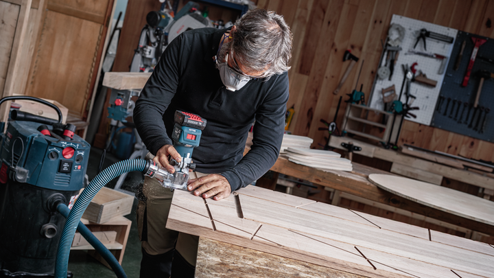 Object #200587698: 7437778_app_web_04 Person wearing safety equipment uses a power tool to rout grooves into a wooden board.