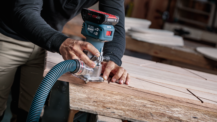Object #200587699: 7437778_app_web_05 Person guides a cordless wood router along a plank in a workshop.