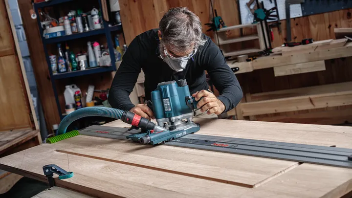 Object #200587713: 7437791_app_web_04 Person wearing safety equipment guides a router along a track to shape a wooden board.