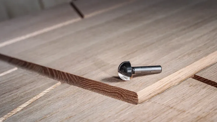Object #200587717: 7437791_app_web_08 Carbide router bit resting on layered wood panel with a freshly cut groove.