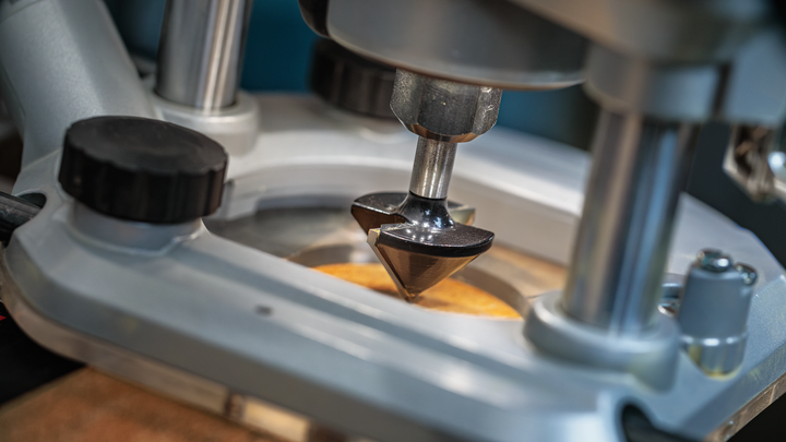 Object #200587727: 7437793_app_web_01 Router bit carving into a wooden surface on a workshop table.