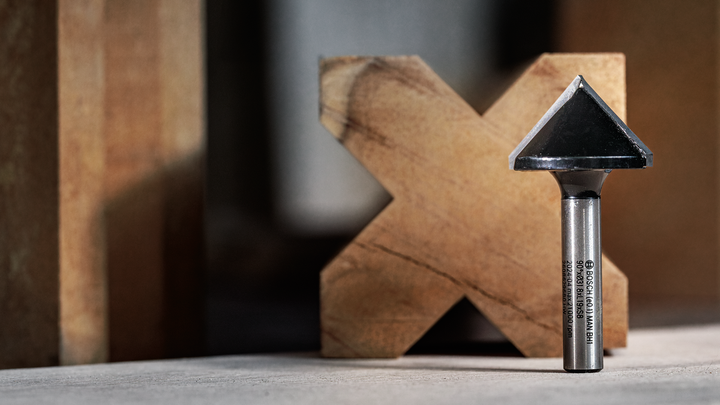 Object #200587733: 7437793_app_web_07 Chamfer router bit standing upright on a workbench in front of a wooden block.