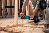 A person wearing safety equipment drills a wooden frame with a cordless angle drill.