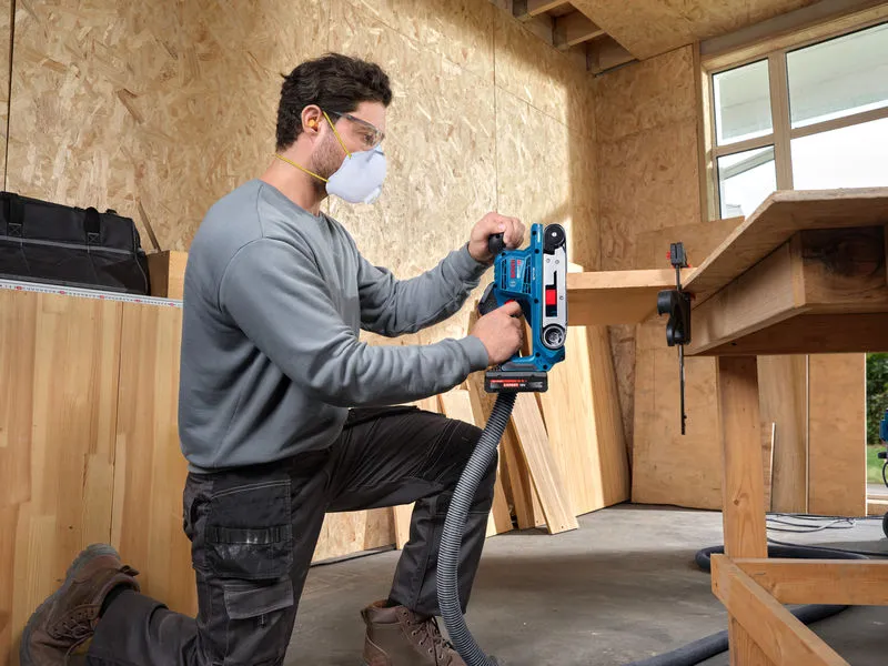 A person wearing safety equipment uses a belt sander on a wooden board.