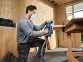 A person wearing safety equipment uses a belt sander on a wooden board.