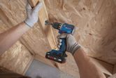 A person wearing safety equipment drills a screw into a wooden panel.