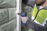 A person wearing safety equipment uses a cordless drill to fasten a bracket on a wall.