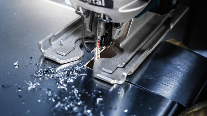 Object #200597843: 2793292_app_web_01 Jigsaw cutting a sheet of metal, small metal shavings scattered around the blade.