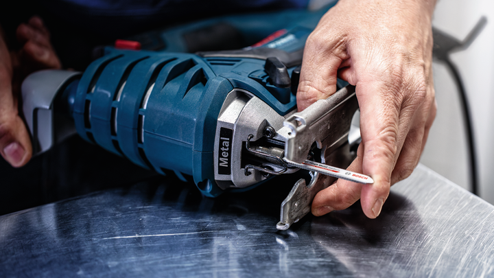Object #200597848: 2793293_app_web_04 Person attaches a jigsaw blade to a power tool on a metal surface.