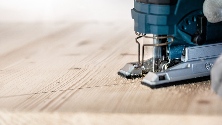 Person guides a jigsaw along a marked line cutting a wooden plank.
