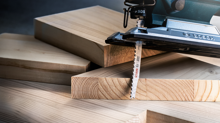 A jigsaw cutting through a thick wooden board.