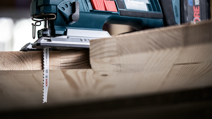 Jigsaw cutting through a thick wooden board in a workshop.