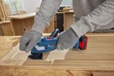 A person wearing safety equipment sands a wooden frame with a multifunction tool.