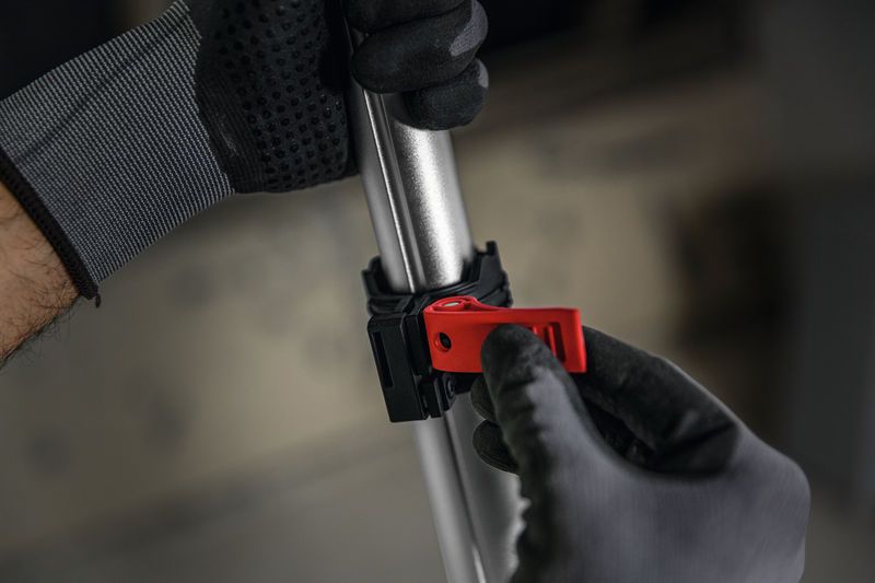 A person wearing safety equipment adjusts a red clamp on a metal pole.