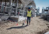 A person wearing safety equipment uses a measuring wheel at a construction site.