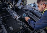 A person wearing safety equipment uses a thermo detector to check engine temperature.