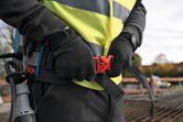 A person wearing safety equipment adjusts a belt with an attached backpack on a construction site.