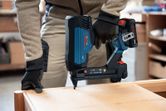 A person wearing safety equipment uses a cordless narrow crown stapler on wood.