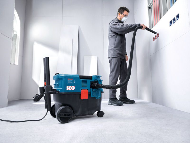 A person wearing safety equipment uses an all-purpose extractor to clean wall outlets.