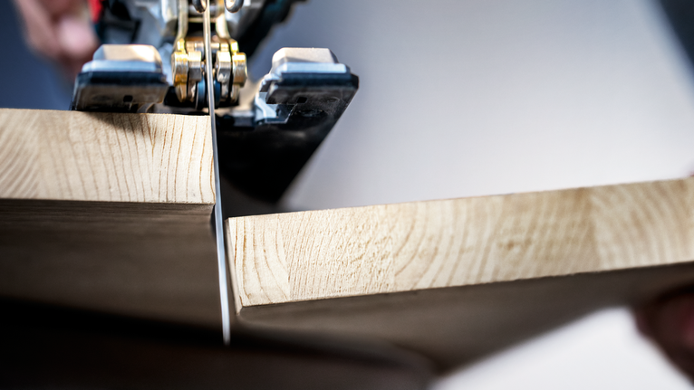 Jigsaw making a precise straight cut through a thick wooden board.
