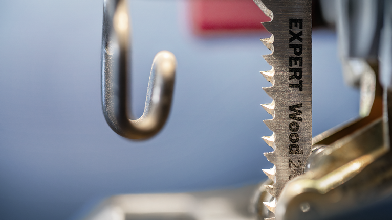 Close-up of a jigsaw blade labeled for wood cutting next to a metal guide.