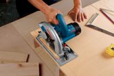A person cuts plywood with a circular saw on a workbench.