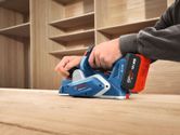 A person smooths a wooden surface with a cordless planer in a workshop.