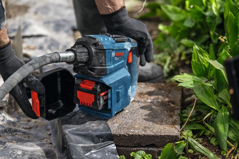 A person wearing safety equipment operates a power tool on a garden stone.