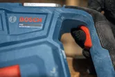 Person wearing safety equipment grips a blue power tool handle with a red trigger.