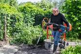 A person wearing safety equipment uses a power tool to mix concrete outdoors.