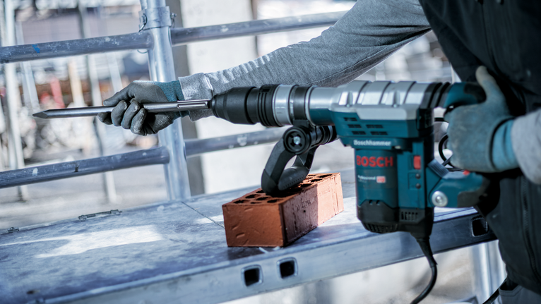 Person wearing safety equipment uses a rotary hammer to chisel a brick.