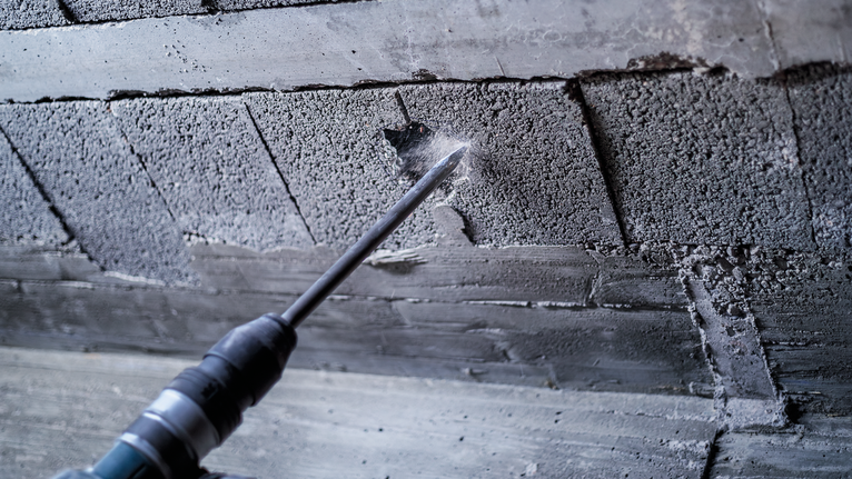 Rotary hammer drilling into a concrete wall, creating dust at the contact point.
