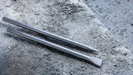 Two metal chisel bits lying on a rough concrete surface.