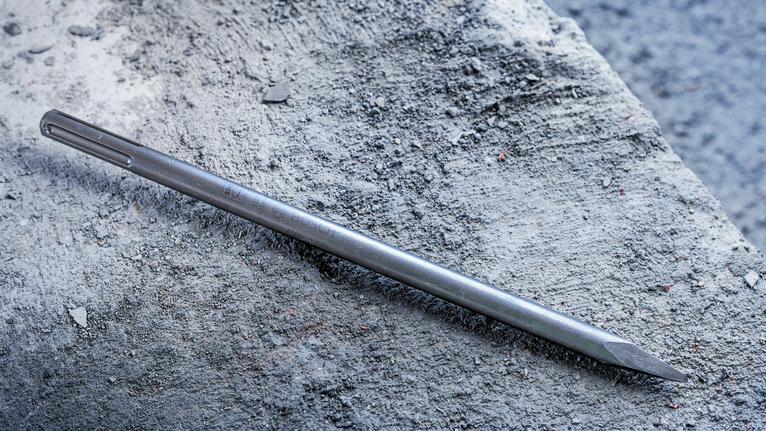 Pointed chisel lying on a rough concrete surface.