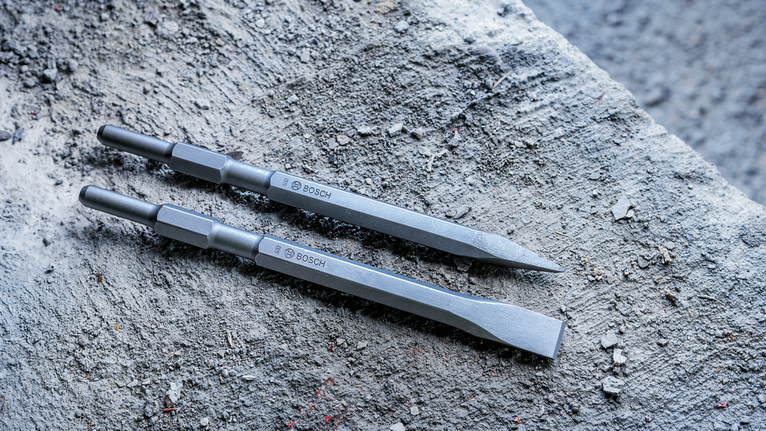 Two metal chisel bits lying on a rough concrete surface.