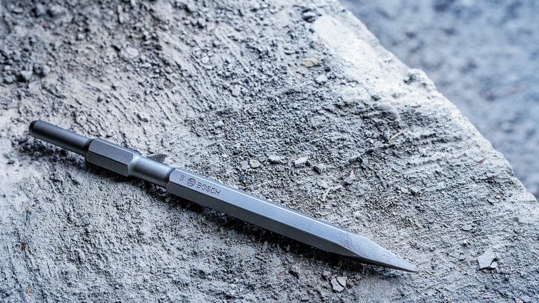 Pointed chisel bit resting on a rough stone surface.