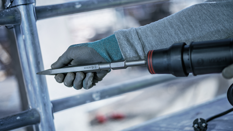 Person wearing safety equipment using a demolition tool with a pointed chisel.