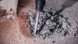 A rotary hammer chisel breaks up concrete rubble on a construction site.